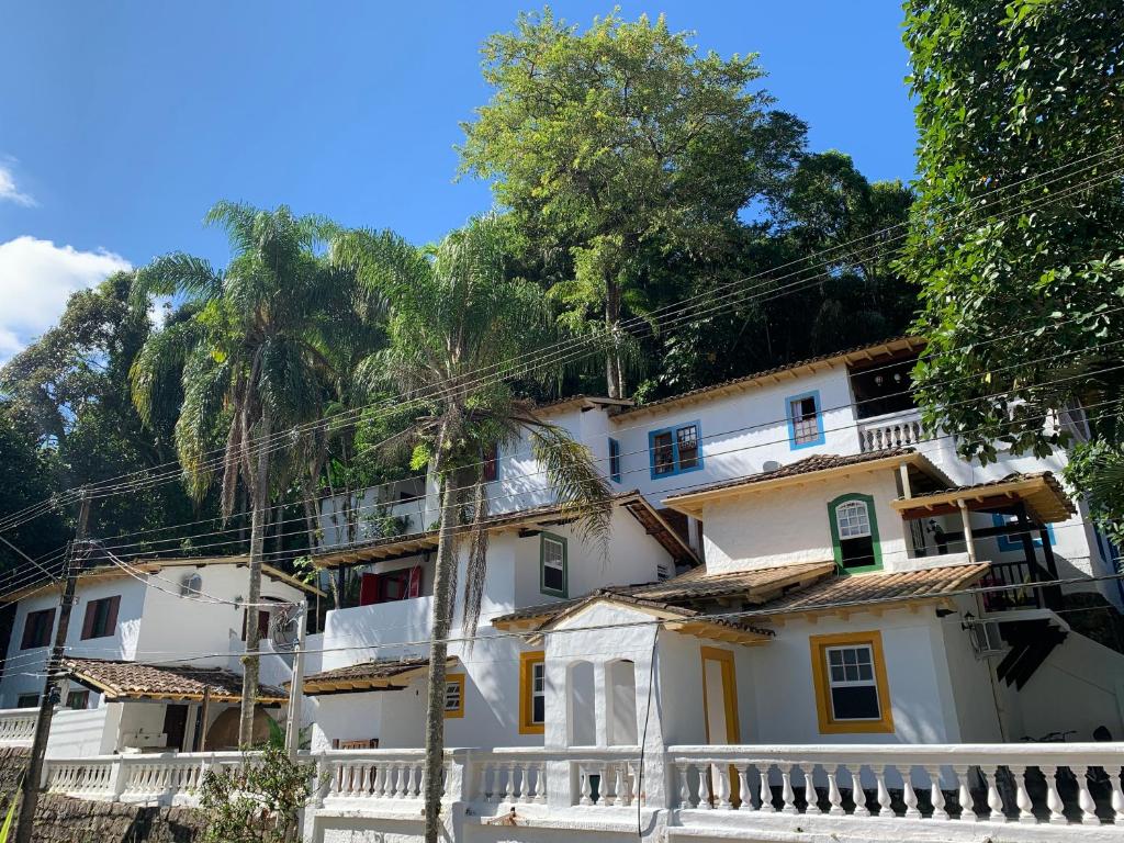 Entrada do Chales Aguas Cantantes, uma construção pintada de branco com janelas amarelas e azul, muitos coqueiros na frente e vegetação