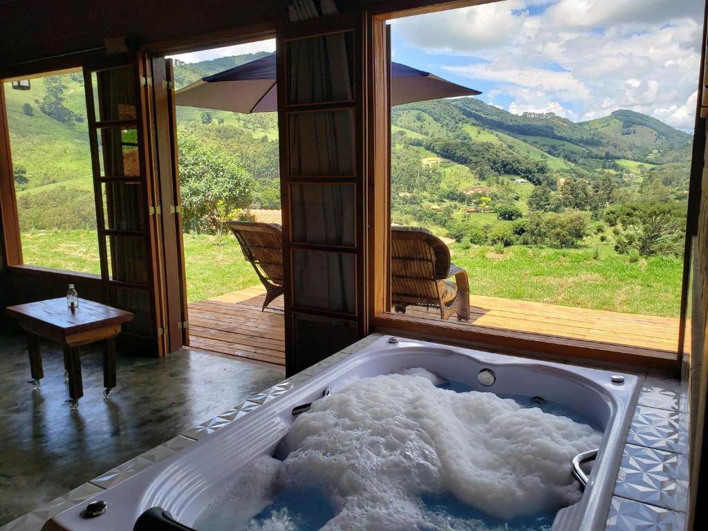 Airbnb em Gonçalves - Hidro no interior do Chalés Bello Neves, e duas janelas grandes de vidro, com vista para as montanhas e para o deck com duas poltronas .