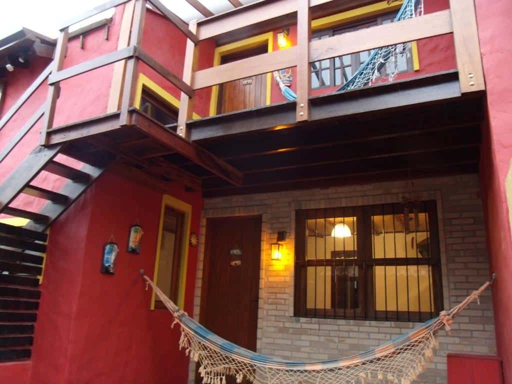 Fachada do Chalés Ubatubaloft, uma acomodação vermelha, com escada de madeira e uma rede na varanda, para representar pousadas na Praia do Tenório