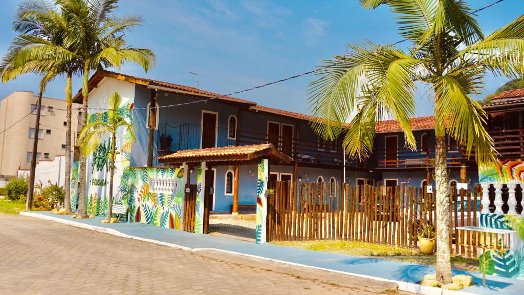 Entrada da Pousada Beija Flor da Praia grande, muro inteiro pintada e decorado com cores do verão e desenho de folhagens, o portão é de madeira e é possível ver o estacionamento interno