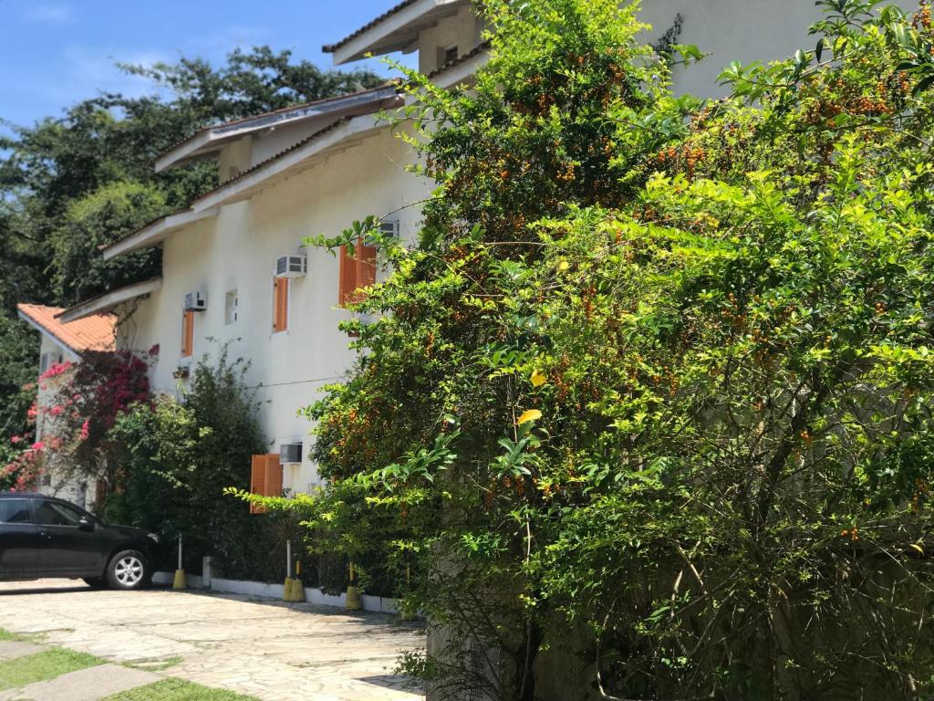 Entrada da Pousada em Villa Encanto, cercada por árvores e muita vegetação, construção branca com detalhes em laranja