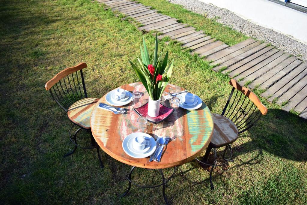 Mesa no jardim em Hospedagem Cristima, uma mesa redonda de madeira com duas cadeiras, um vaso de flor, alguns pratos e xícaras brancos