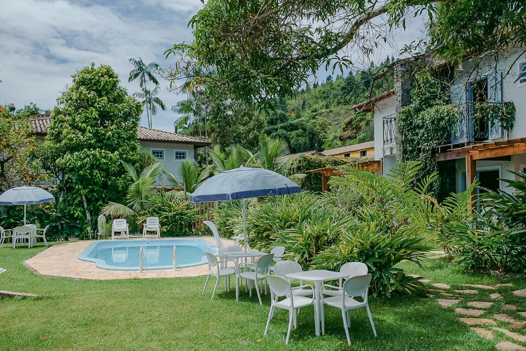 Jardim na Villa Divina Pietra – Ubatuba, uma piscina, muita vegetação ao redor, cadeiras, guarda-sóis e espreguiçadeiras no deck