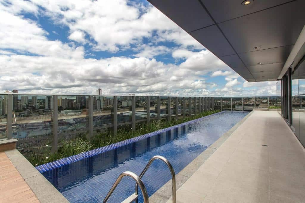 Piscina de borda infinita, com paredes de vidro e vista para a cidade e céu azul de Curitiba