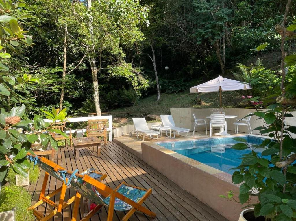 Piscina do Bougainville Toque Toque Grande, um local com cadeiras e espreguiçadeiras, uma piscina quadrada, um deck de madeira com cadeiras e mesinhas, e m guarda-sol, ao redor, muita vegetação