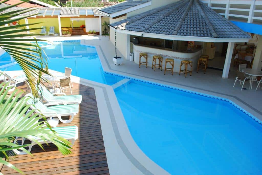 Piscina do Ciribaí Praia Hotel em Toque Toque, uma piscina ampla, ao redor, de um dos lados tem um deck com espreguiçadeiras, do outro, um pequeno bar com algumas cadeiras