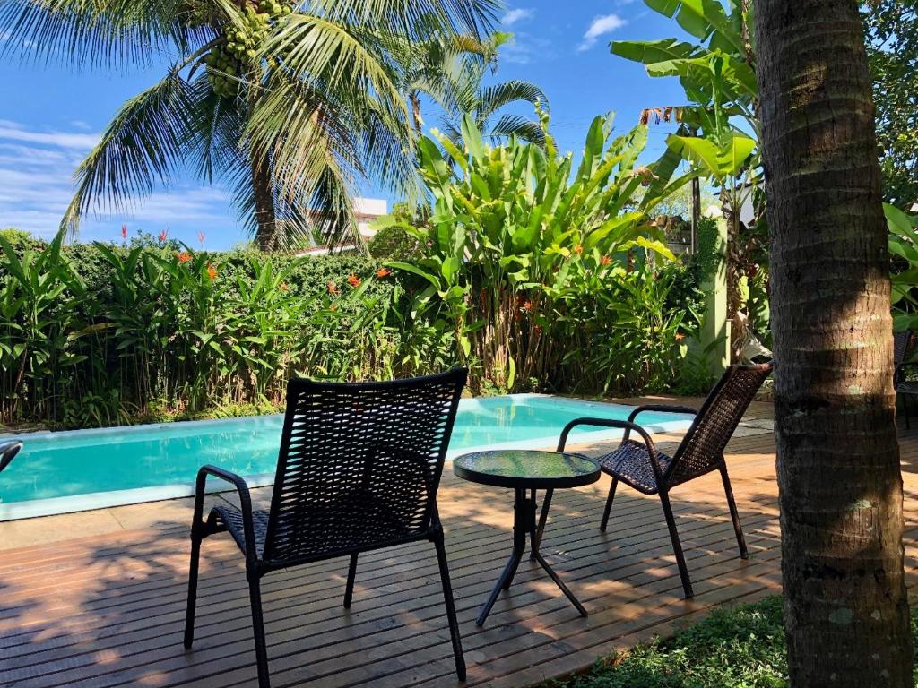 Área externa da  Jataí Guest House, uma piscina cercada por muita vegetação e um deck com mesa e cadeiras