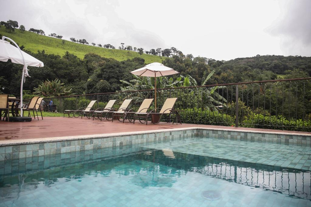 Piscina externa da Pousada Vila do Lago com águas claras, espreguiçadeiras e guarda-sóis à beira da piscina; colinas verdes e árvores ao fundo.