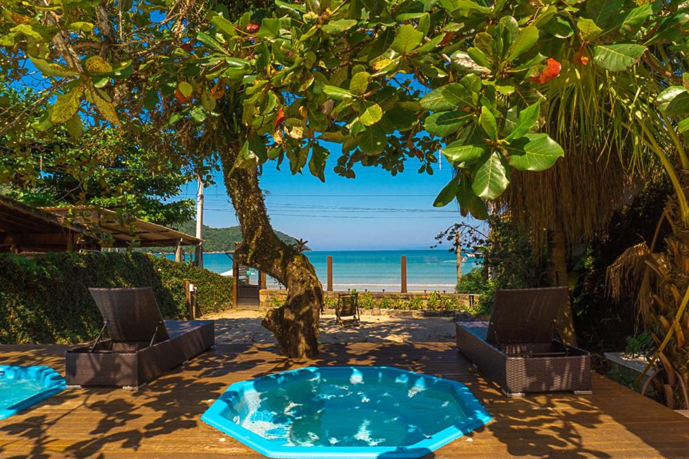 Pequena piscina na Pousada Vila Jacaa, virada para a praia da Enseada em Ubatuba, com duas cadeiras sob o deck e muitas árvores ao redor