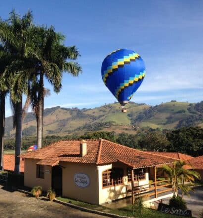 A entrada da Pousada Le Sapê, com montanhas ao fundo e um balão azul sobrevoando a propriedade