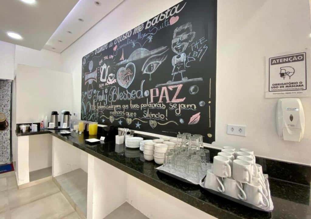 Pousada Mar Suites, local do café da manhã, com uma bancada com utensílios de cozinha e um quadro negro com desenhos coloridos e mensagens positivas