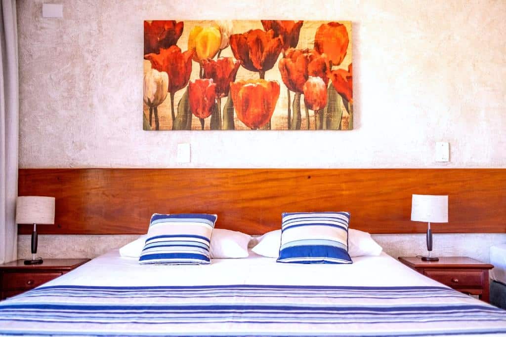 Quarto em Pousada NAAN Lázaro Ubatuba, uma cama de casal, uma quadro com flores sob a cama, duas cabeceiras com abajur, duas almofadas azuis, para representar airbnb em Ubatuba