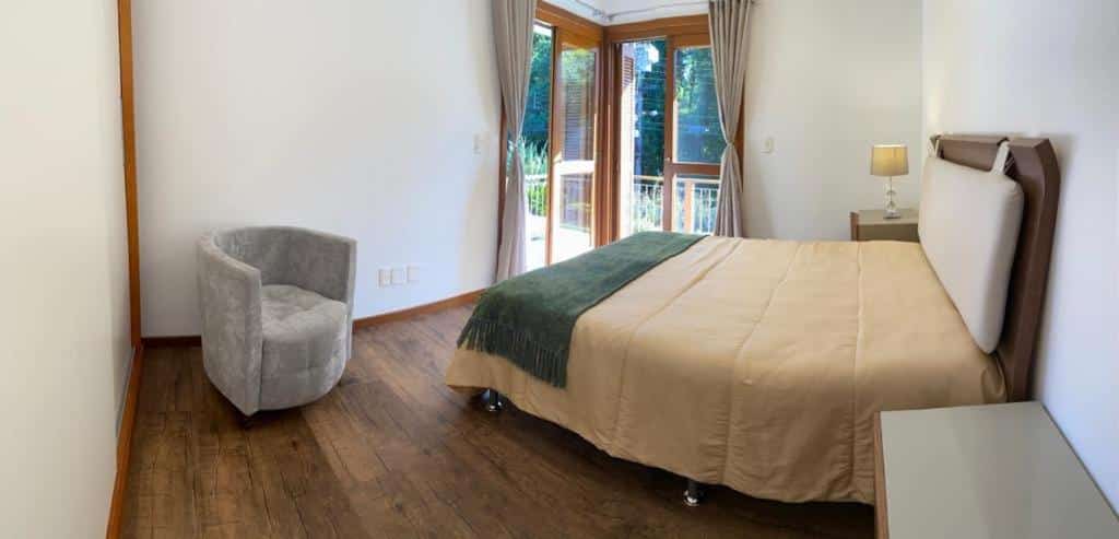 Um quarto 3 QUARTOS PRÓXIMO AO CENTRO, uma cama de casal, uma pequena poltrona, uma sacada ampla com cortinas, para representar airbnb em Gramado