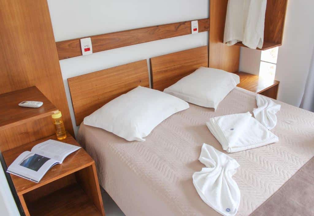 Quarto do Alapage Toque Toque, uma cama de casal, com toalhas e travesseiros sob a cama, estantes de madeira ao redor, para representar pousadas em São Sebastião