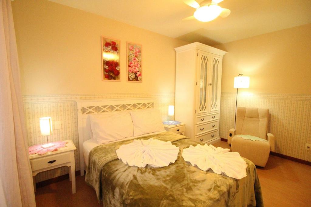 Quarto no Araucárias 302, uma cama de  casal, uma poltrona, um abajur, um armário, dois quadros e uma janela, para representar airbnb em Gramado