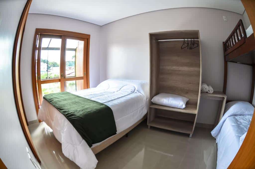 Quarto na Casas dos Alpes, uma cama de casal, uma beliche, uma sacada, um armário de conceito aberto, para representar airbnb em Gramado