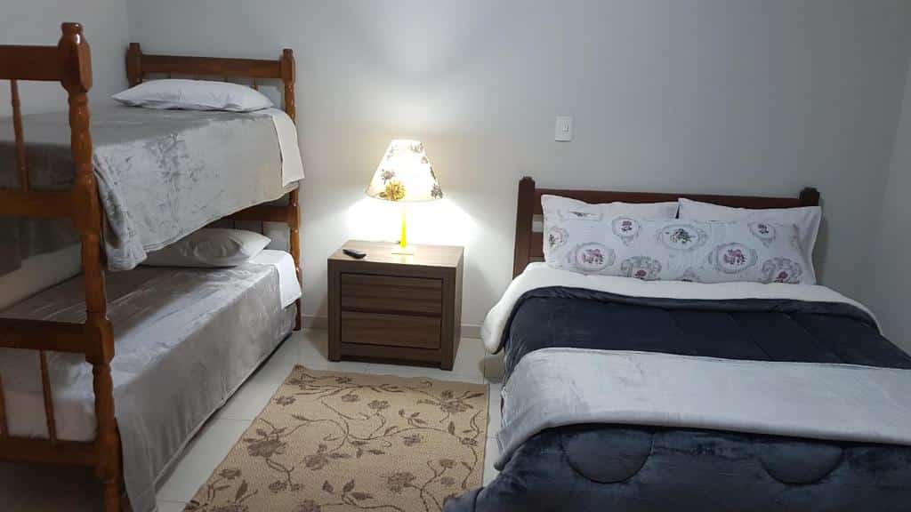 Quarto na Casa Campos, uma cama de casal e uma beliche, uma mesinha com um abajur entre as duas camas, para representar airbnb em Campos do Jordão