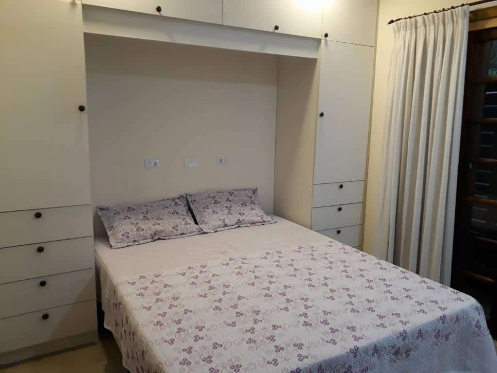 Quarto na Casa Centro de Ubatuba, uma cama de casal, uma sacada e um armário com gavetas ao redor, para representar pousadas no Centro de Ubatuba