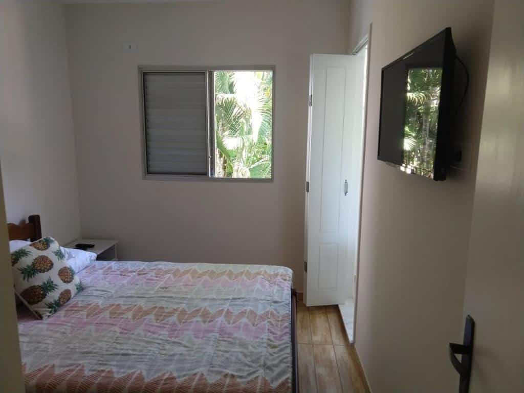 Quarto da Casa na Toninhas, uma cama de casal, uma televisão e uma janela, para representar airbnb na Praia das Toninhas em Ubatuba