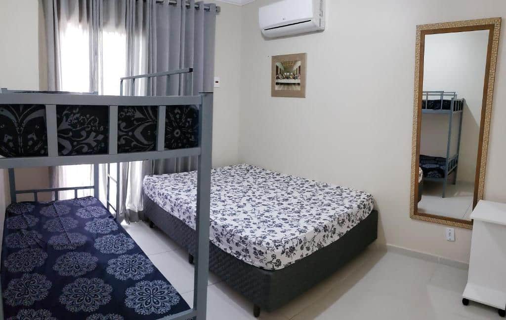 Quarto na Casa Melo 4, uma cama de casal, uma beliche, uma sacada, um espelho e um pequeno móvel, para representar airbnb em Ubatuba