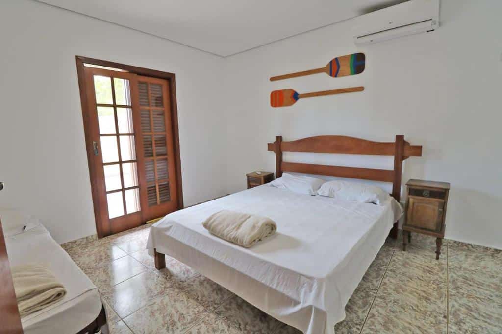Quarto na Casa Vip Ubatuba - Vista para o Mar - Praia das Toninhas, uma cama de casal, um ar-condicionado, dois pequenos móveis ao lado da cama, e a porta de uma sacada, para representar airbnb na Praia das Toninhas em Ubatuba