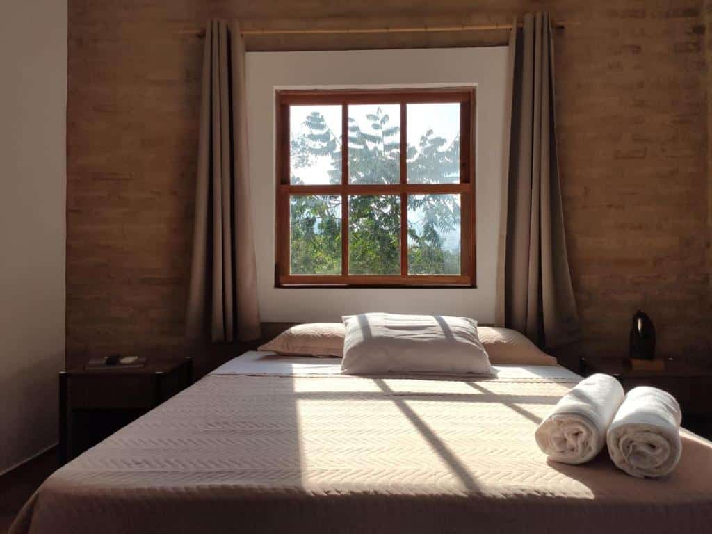 quarto com uma cama de sal com duas toalhas logo abaixo de uma ampla janela com vista para a natureza da serra da canastra.