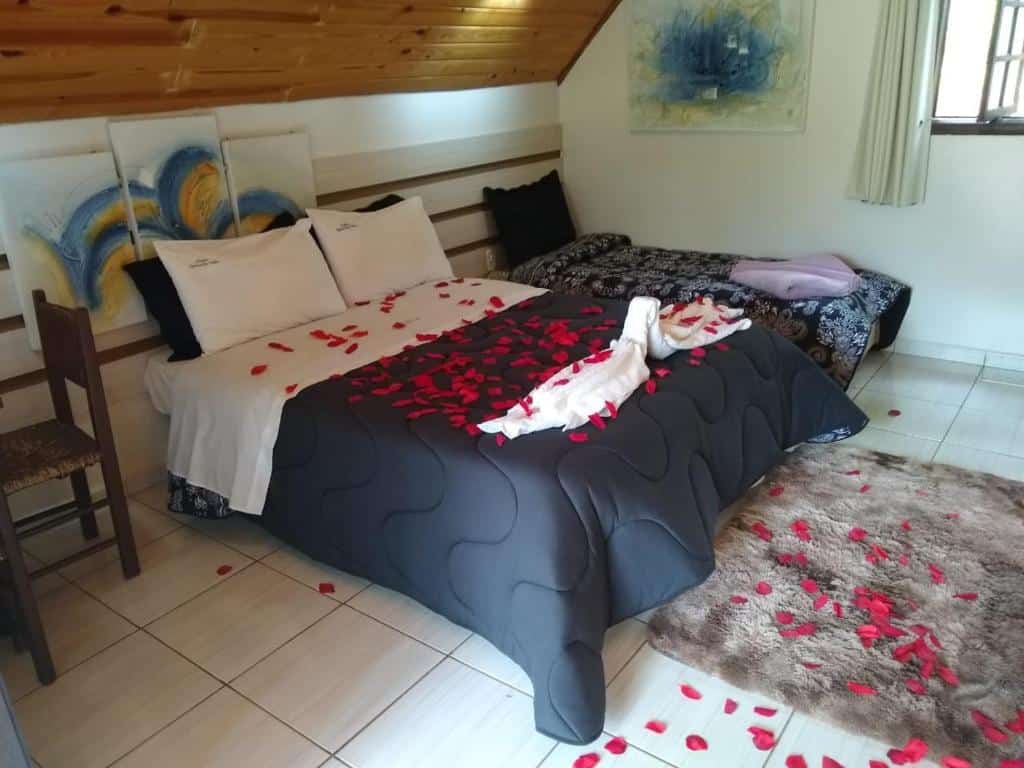 Quarto no Chalés Praia de Minas, uma cama de casal e uma de solteiro, com travesseiros, toalhas, um tapete e uma janela com cortinas, para representar pousadas em São Lourenço