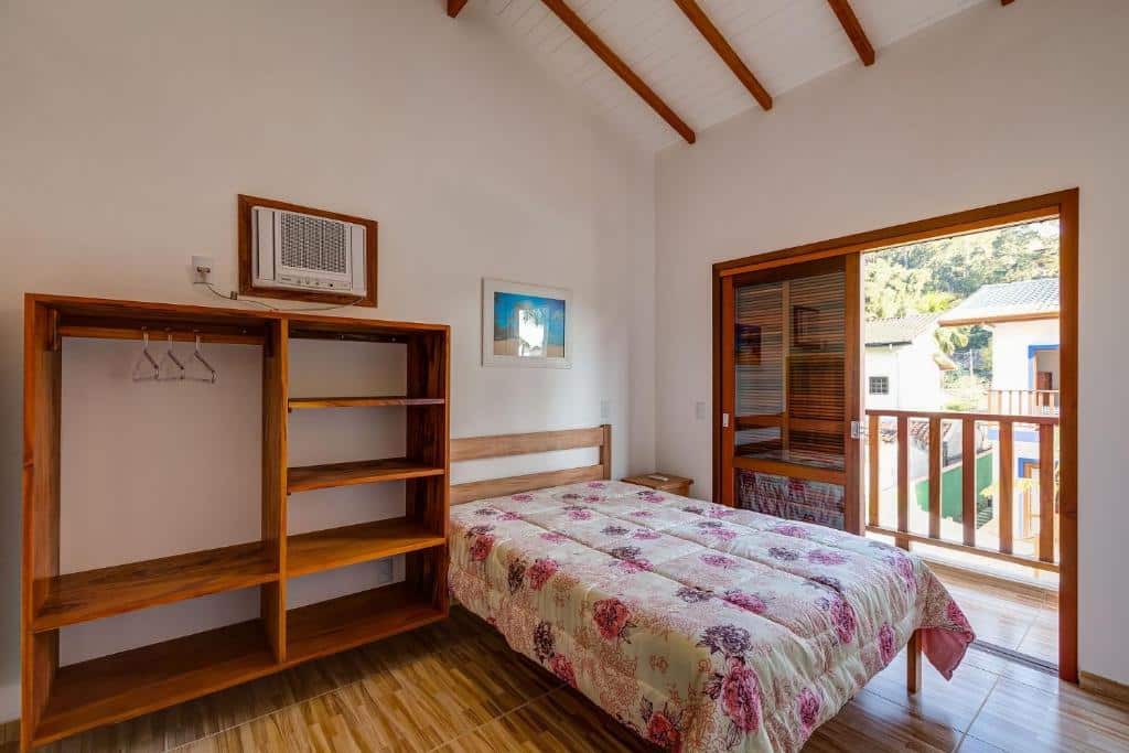 Quarto em Condomínio na Praia do Lázaro, uma cama de casal, uma sacada ampla com vista para o jardim, um armário de conceito aberto de madeira, um ar-condicionado, para representar airbnb na Praia do Lázaro
