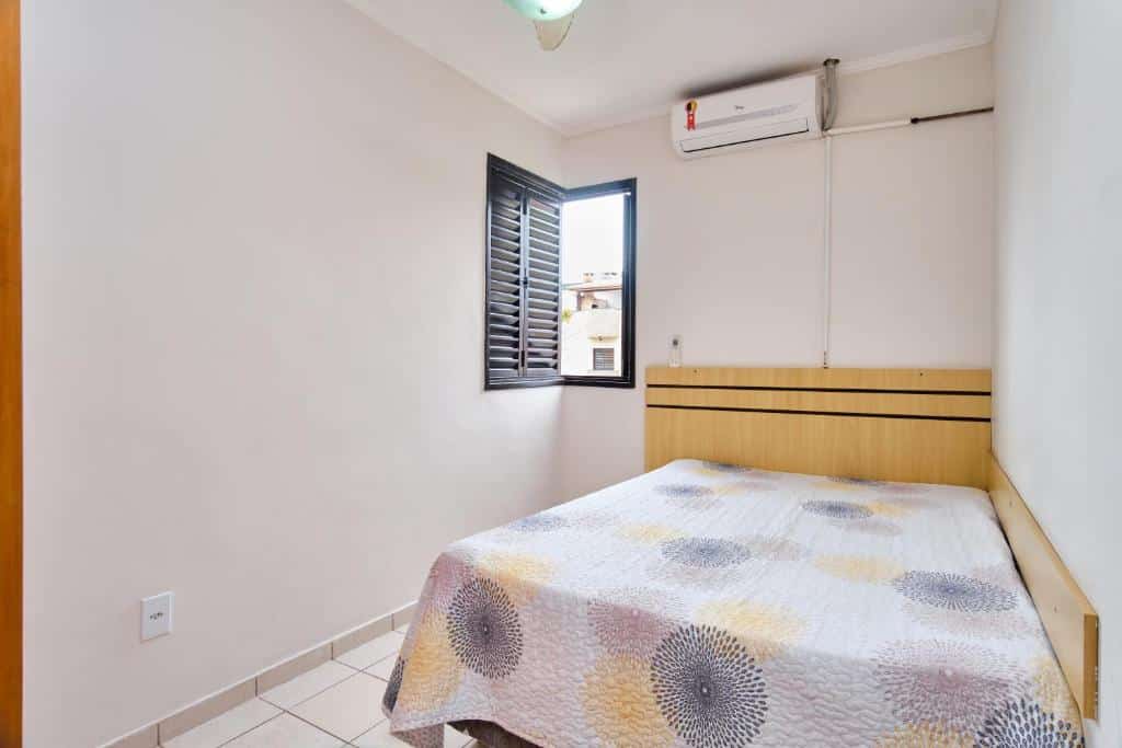 Quarto no Fabiano Ubatuba, uma cama de casal, uma janela e um ar-condicionado, para representar pousadas na Praia do Tenório