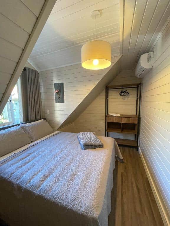 Um quarto no  Family House Gramado, um armário de conceito aberto, um lustre. um ar-condicionado, uma janela e uma cama de casal, para representar airbnb em Gramado