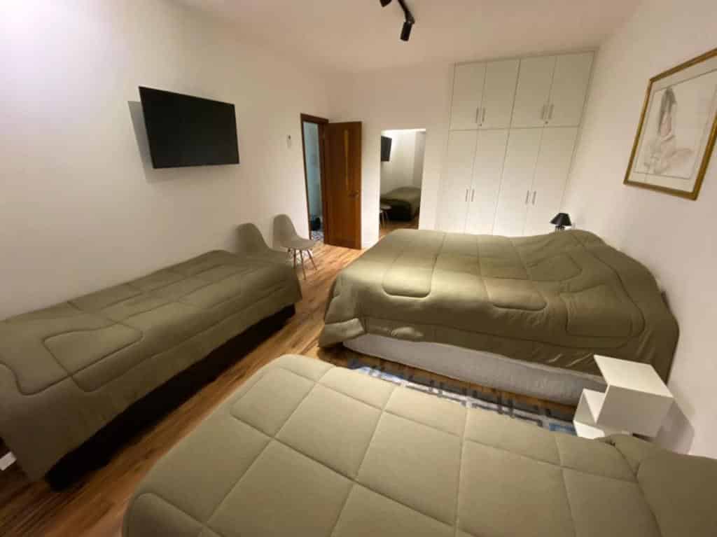 Quarto do Apartamento Campos do Jordao Home Green Home, local amplo, uma cama de casal, duas de solteiro, uma televisão, armários embutidos, duas cadeiras e uma espelho, para representar airbnb em Campos do Jordão