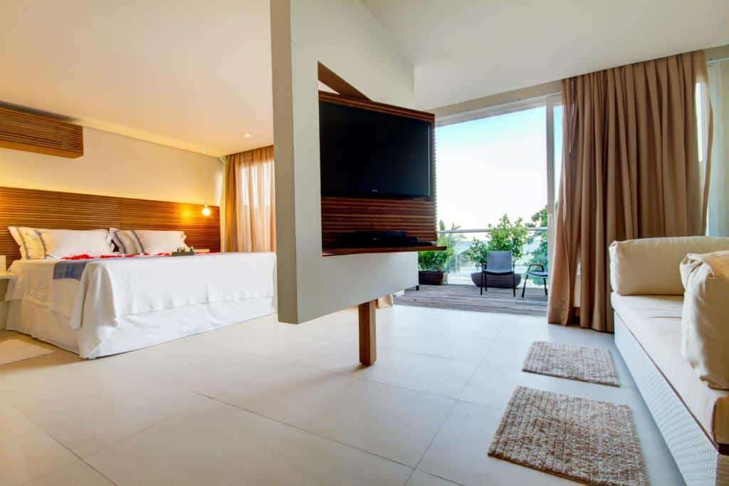 Quarto no  Hotel Spa Nau Royal, tudo novo e moderno, uma televisão ampla, uma cama de casal, um sofá, uma enorme sacada com vista para o mar, para representar pousadas em São Sebastião