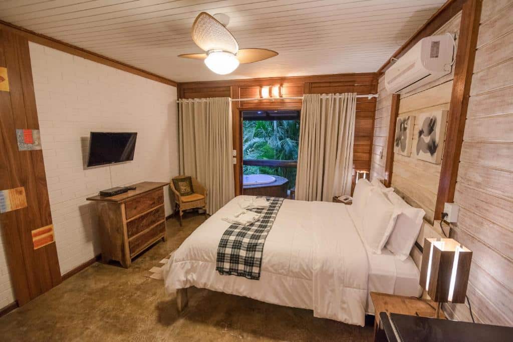 Quarto de luxo em Ilha de Toque Toque Boutique Hotel & Spa, com uma hidromassagem na área da sacada, uma cama de casal, um ar-condicionado, uma cômoda e uma cadeira de madeira e uma televisão