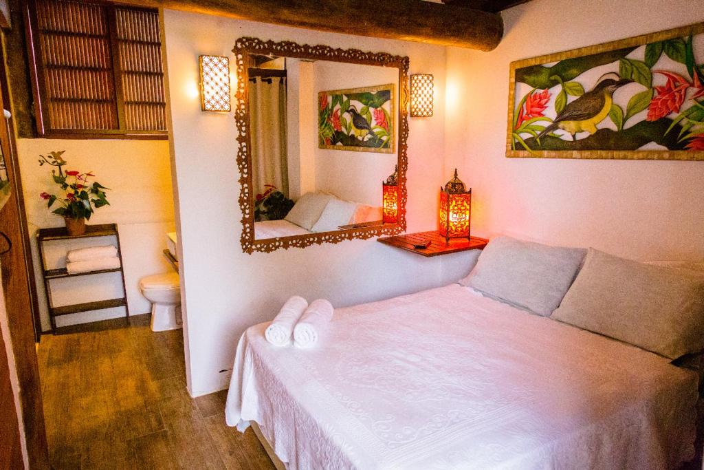 Quarto em  Itamambuca Casa das ondas, uma cama de casal, um espelho, um banheiro e móveis rústicos, decoração que remete ao bambu e a madeira, para representar airbnb em Ubatuba