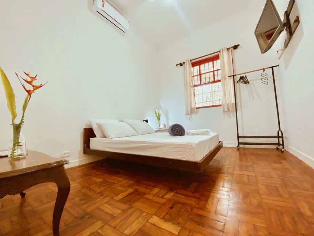 Quarto em  Jataí Guest House, uma cama de casal, chão de taco, um ar-condicionado, um cabideiro, uma janela e uma televisão, para representar pousadas no Centro de Ubatuba