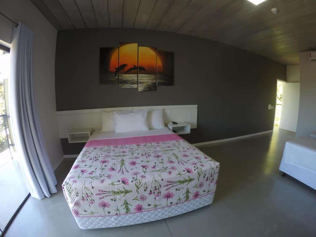 Quarto na Luz da Lua Pousada, uma cama de casal, um quarto amplo, um quadro sob a cama, uma sacada com cortinas, para representar pousadas na Praia do Sapê em Ubatuba