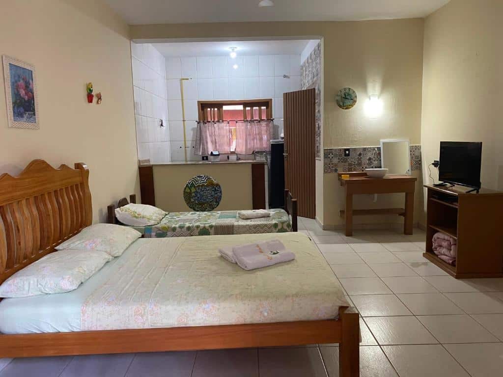 Vista do quarto da Pousada Chales Madu com camas, televisão e cozinha simples.