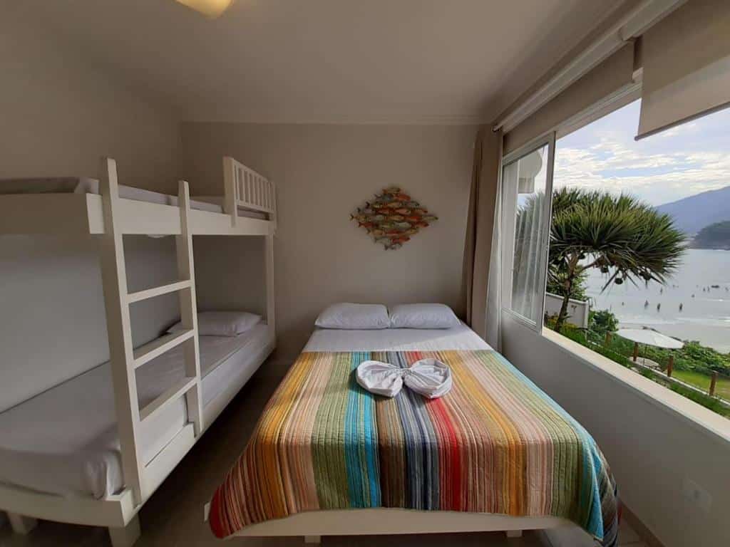 Quarto do MANSÃO TENÓRIO - Suítes, Estudio ou Cobertura Pé na Areia, uma cama de casal com uma janela ampla dando vista para a praia, para representar pousadas na Praia do Tenório
