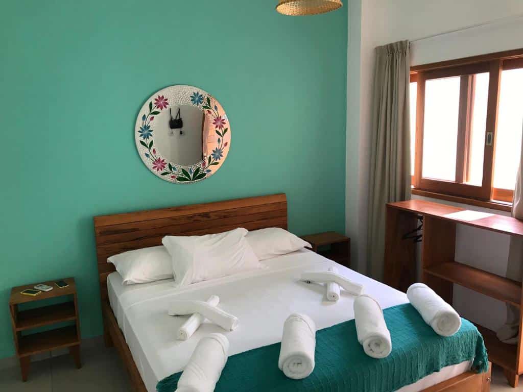 Quarto em Nai'a Suites, uma cama de casal com toalhas em cima, travesseiros, um espelho redondo, algumas prateleiras e uma pequena cômoda