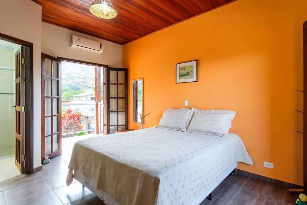 Quarto na CASA LINDA E ESPAÇOSA COM AR - 50 MTS DA PRAIA, uma cama de casal, uma varanda, um ar-condicionado, um cabideiro, para representar airbnb em Ubatuba