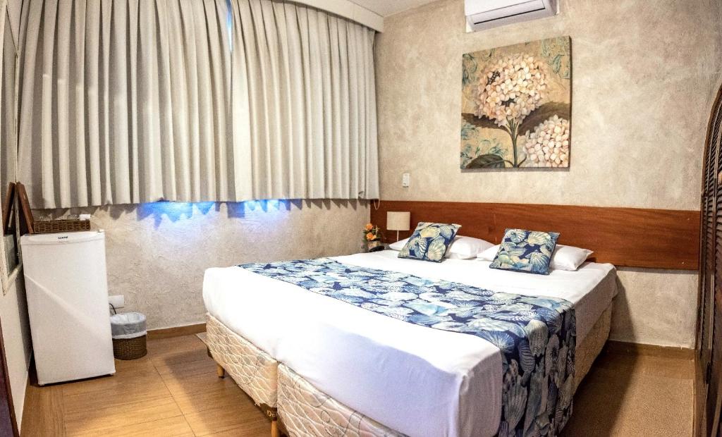 Quarto na Pousada NAAN Lázaro Ubatuba, uma quarto decorado com uma cama de casal, frigobar, janela com persiana, um quadro sob a cama e ar-condicionado