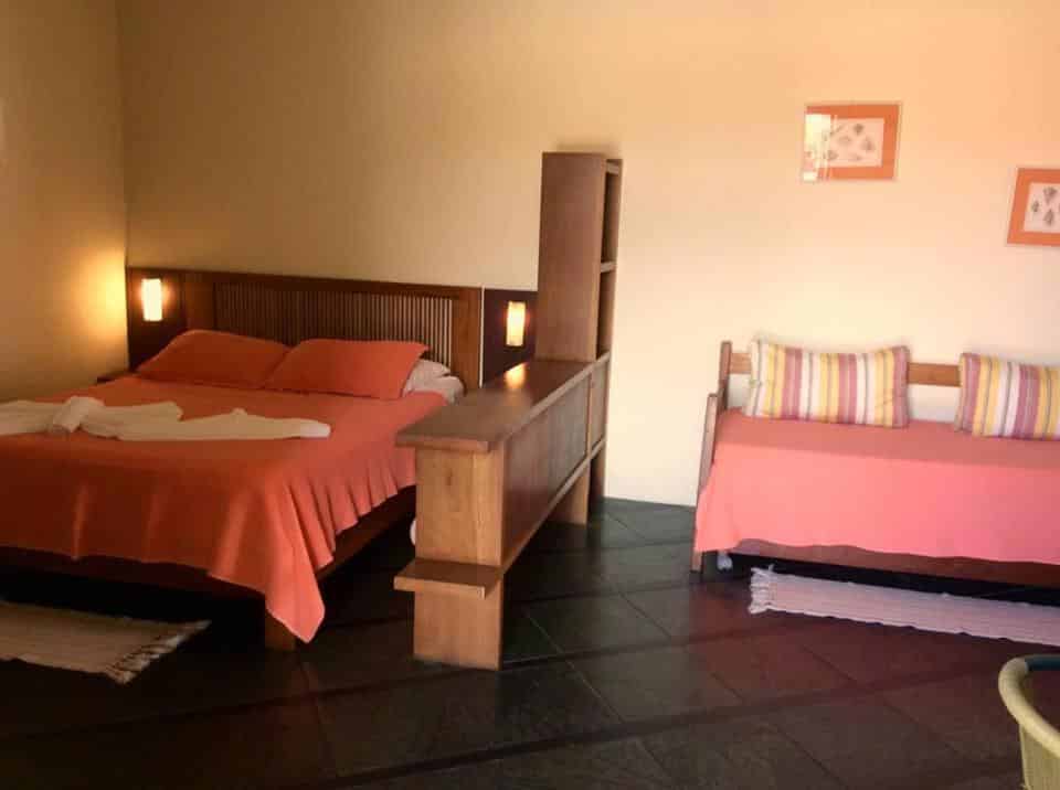 Quarto em Pousada Refugio Port Sahy, uma cama de casal e um pequeno sofá, quadros, almofadas e travesseiros em tom de laranja, pousadas na Barra do Sahy