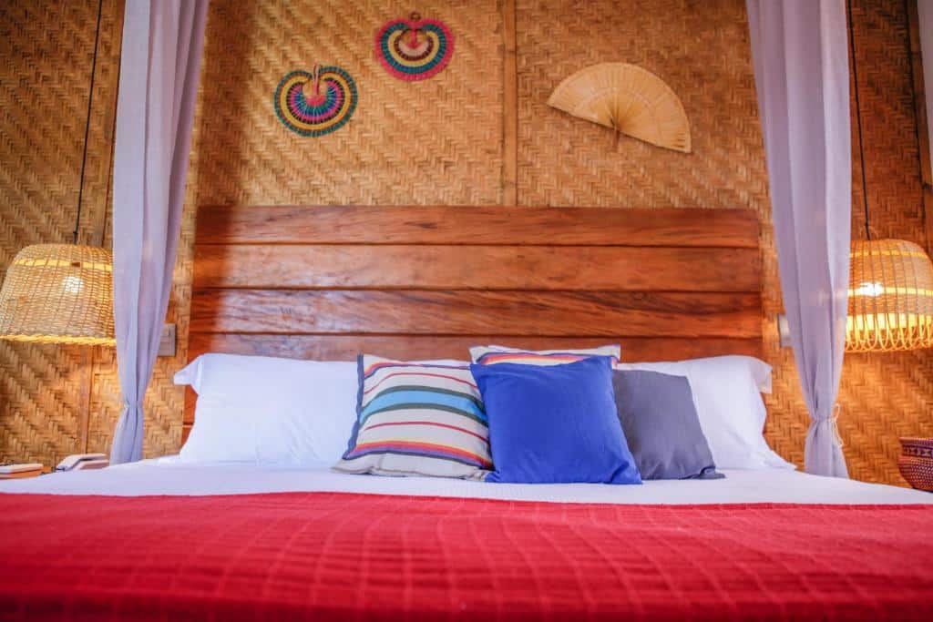 Quarto em Pousada TeMoana, uma local rústico e estiloso, com tudo de madeira e palha, uma cama de casal com almofadas coloridas e dois abajures de palha