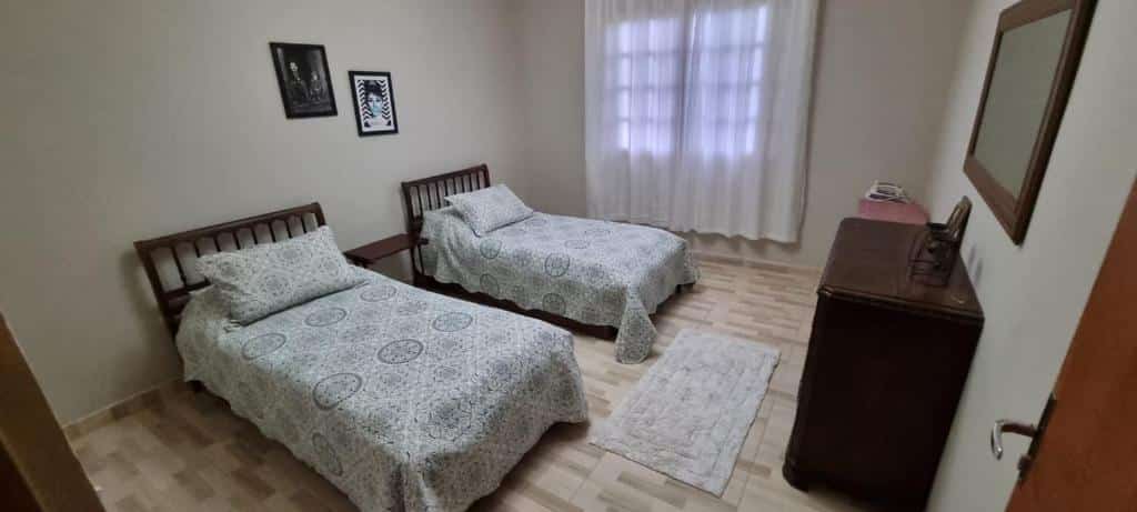 Quarto no Refugio em Campos, duas camas de solteiro, uma cômoda, uma janela com cortinas, uma espelho, para representar airbnb em Campos do Jordão