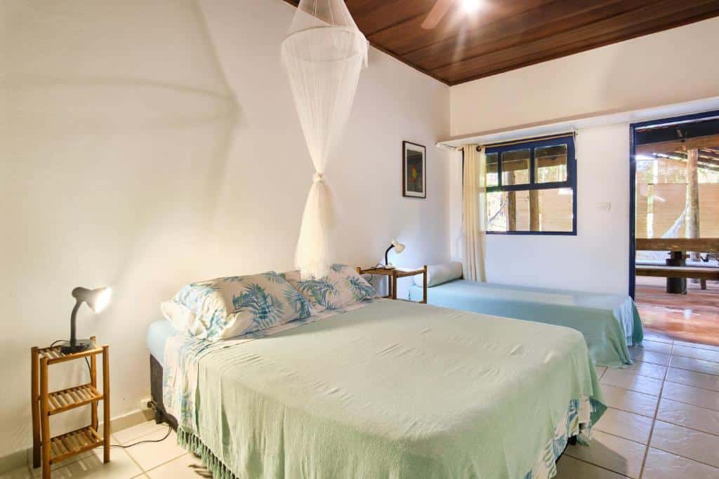 Quarto no Residence Picinguaba, uma cama de casal e uma de solteiro, uma sacada, dois abajures e mesinhas de bambu