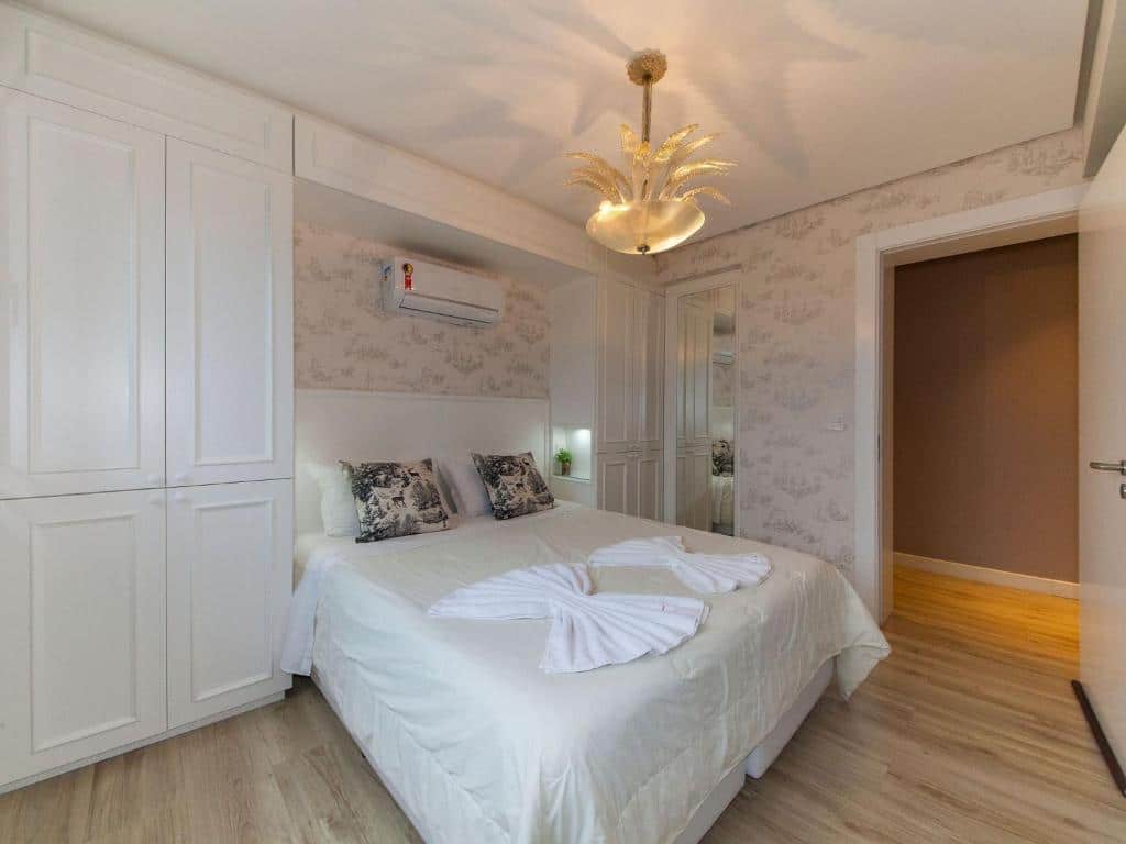 Quarto no Residencial Via Florida Gramado, uma cama de casal com toalhas e almofadas em cima, dois armários embutidos, um ar-condicionado, para representar airbnb em Gramado