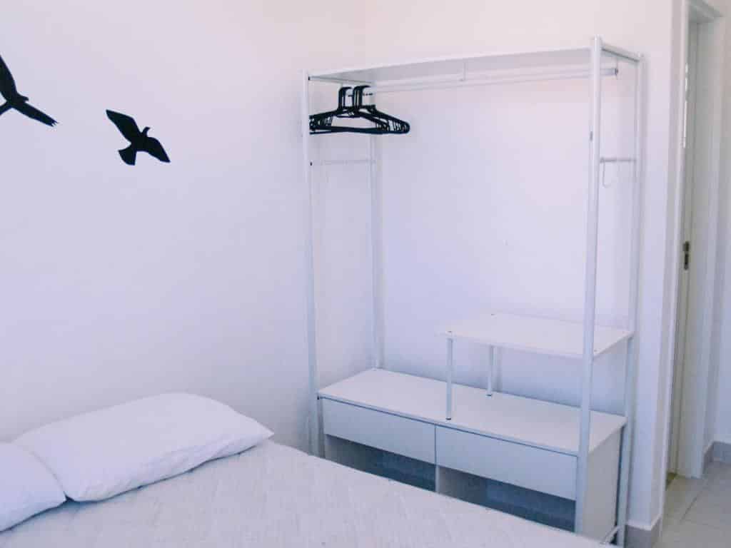 Quarto no Rubi 406 - 200 mts da praia, uma cama de casal e um móvel com conceito de armário aberto, com gavetas e prateleiras, para representar airbnb na Praia das Toninhas em Ubatuba