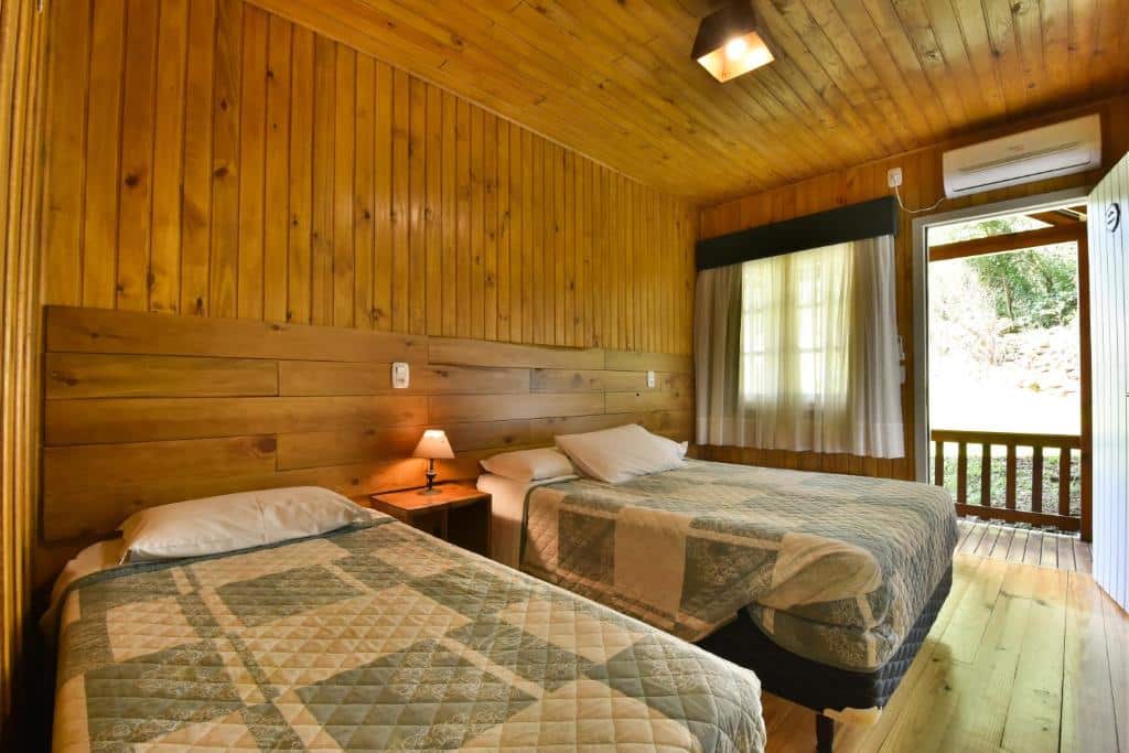 Quarto no Stillo Gramado Bella Itália, duas camas de solteiro, uma mesinha com um abajur entre as duas camas, um ar-condicionado, uma janela e uma pequena varanda, para representar airbnb em Gramado