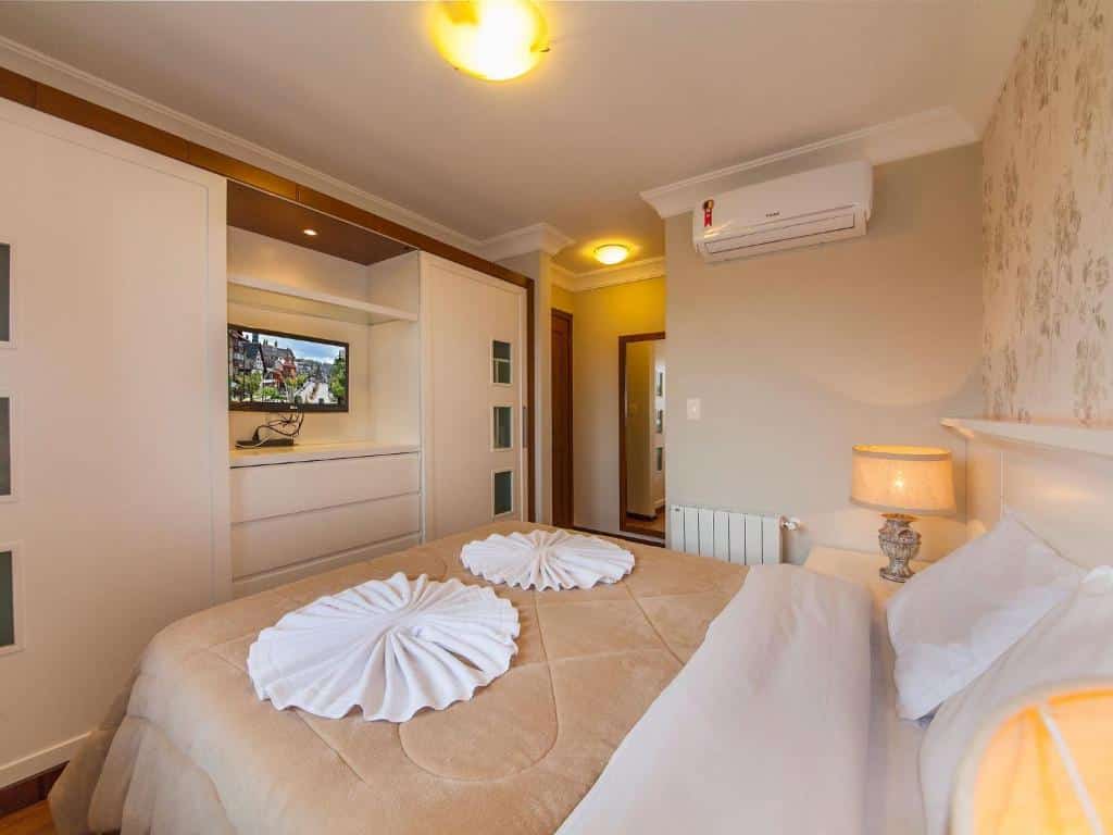 Quarto na Villa Di Pietro - 404, uma cama de casal, um abajur sob uma mesinha, um ar-condicionado, uma armário embutido com uma televisão, para representar airbnb em Gramado