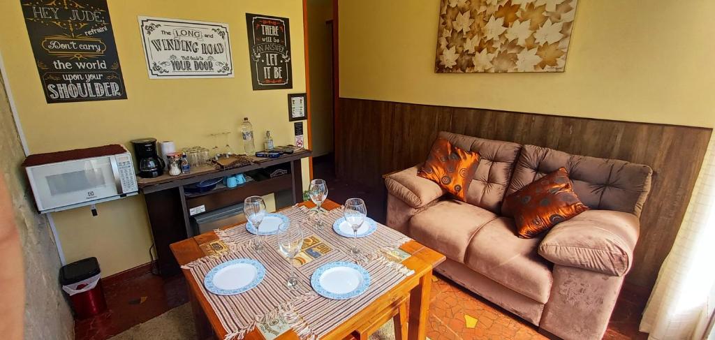 Sala de estar no Recanto do Sonho em Campos do Jordão, um sofá, umas mesa com quatro lugares, uma estante com alguns utensílios de cozinha